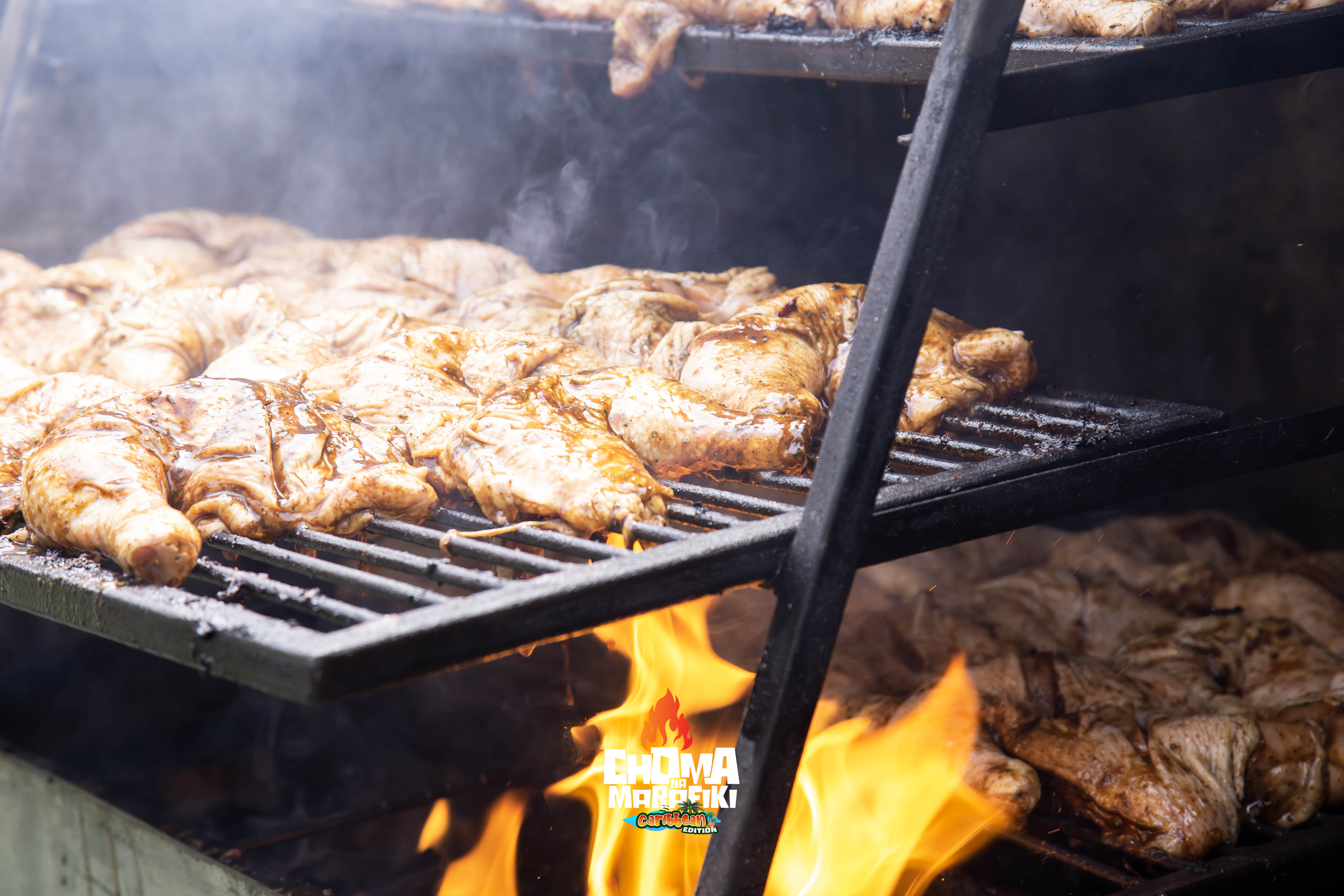 Basting marinated chicken pieces on a large grill at Caribbean Edition