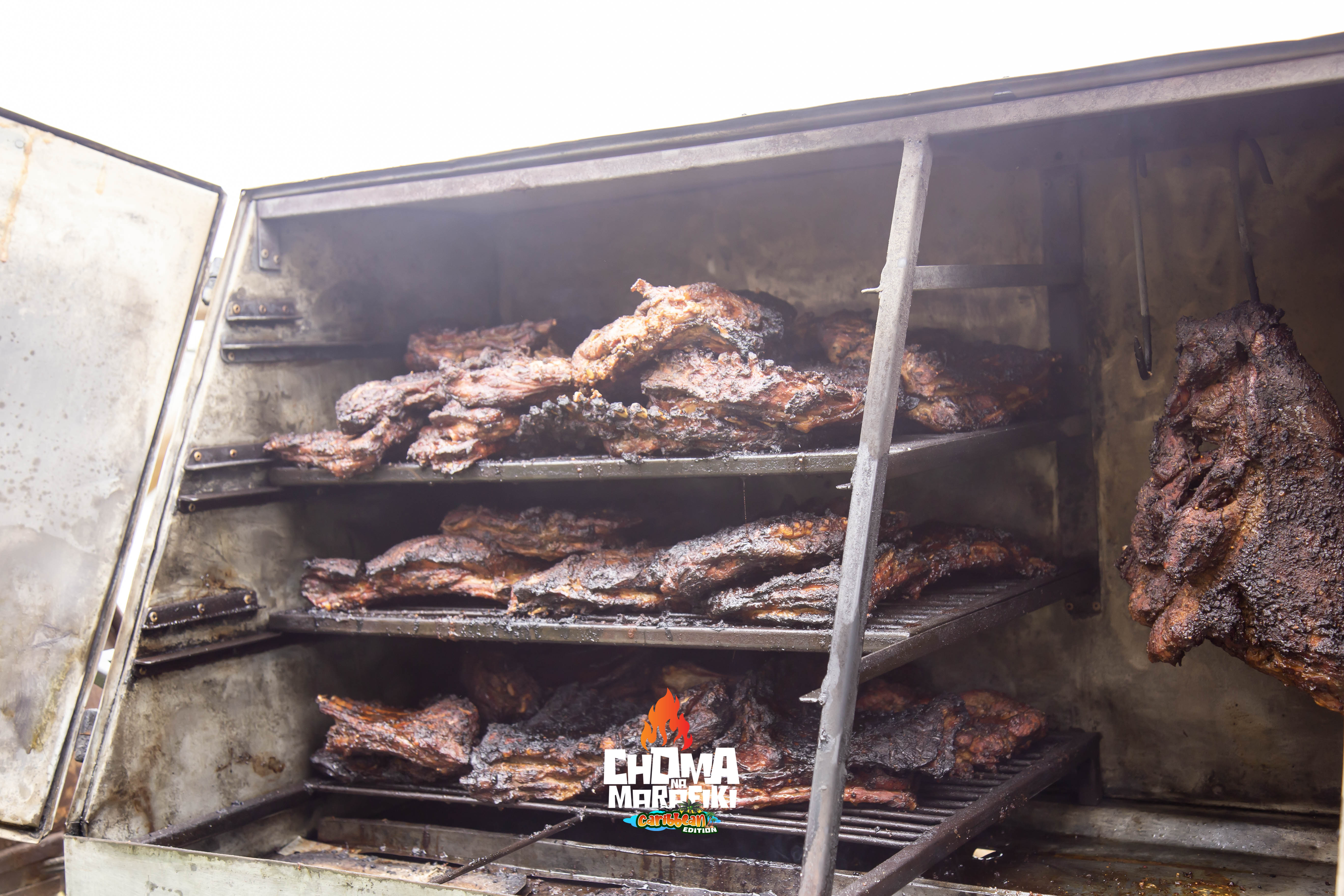 Multiple racks of ribs inside open smoker at Choma Na Marafiki Caribbean Edition
